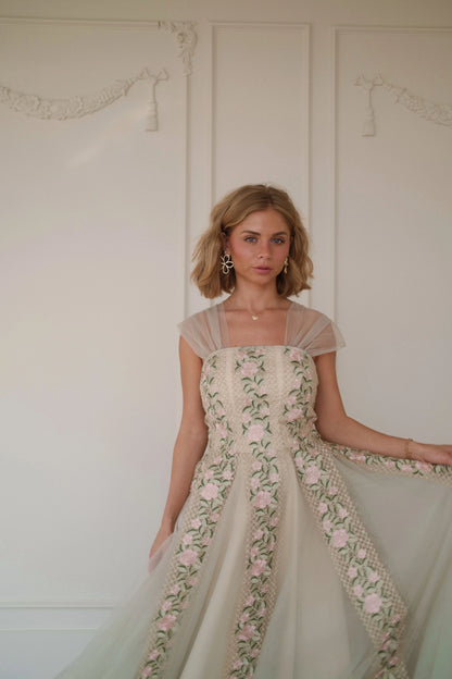 Woman in a white floral dress with short sleeves and a full skirt poses against a white wall.