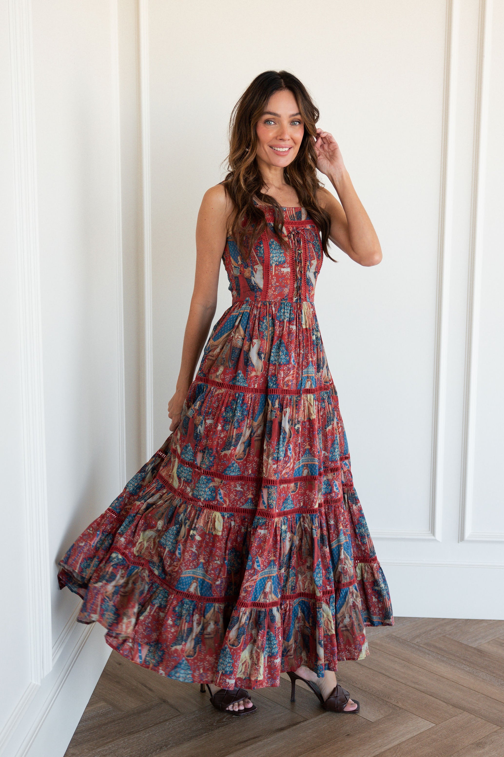 A woman standing in front of a mirror wearing a beautiful, long, red, blue, and black dress. The dress is from the brand Lola and is perfect for a wedding.