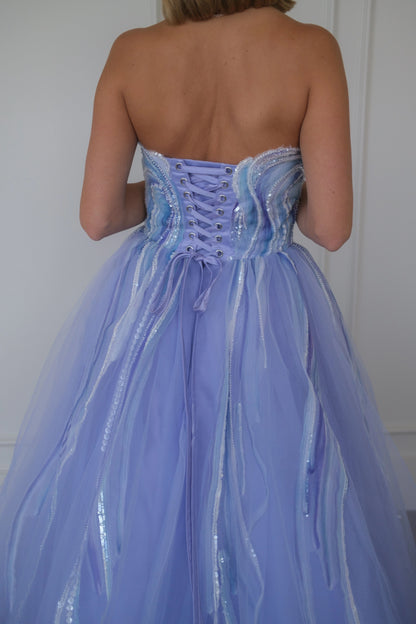 Woman wears a strapless lilac ballgown with corset back and tulle skirt with shiny stripes, facing away.