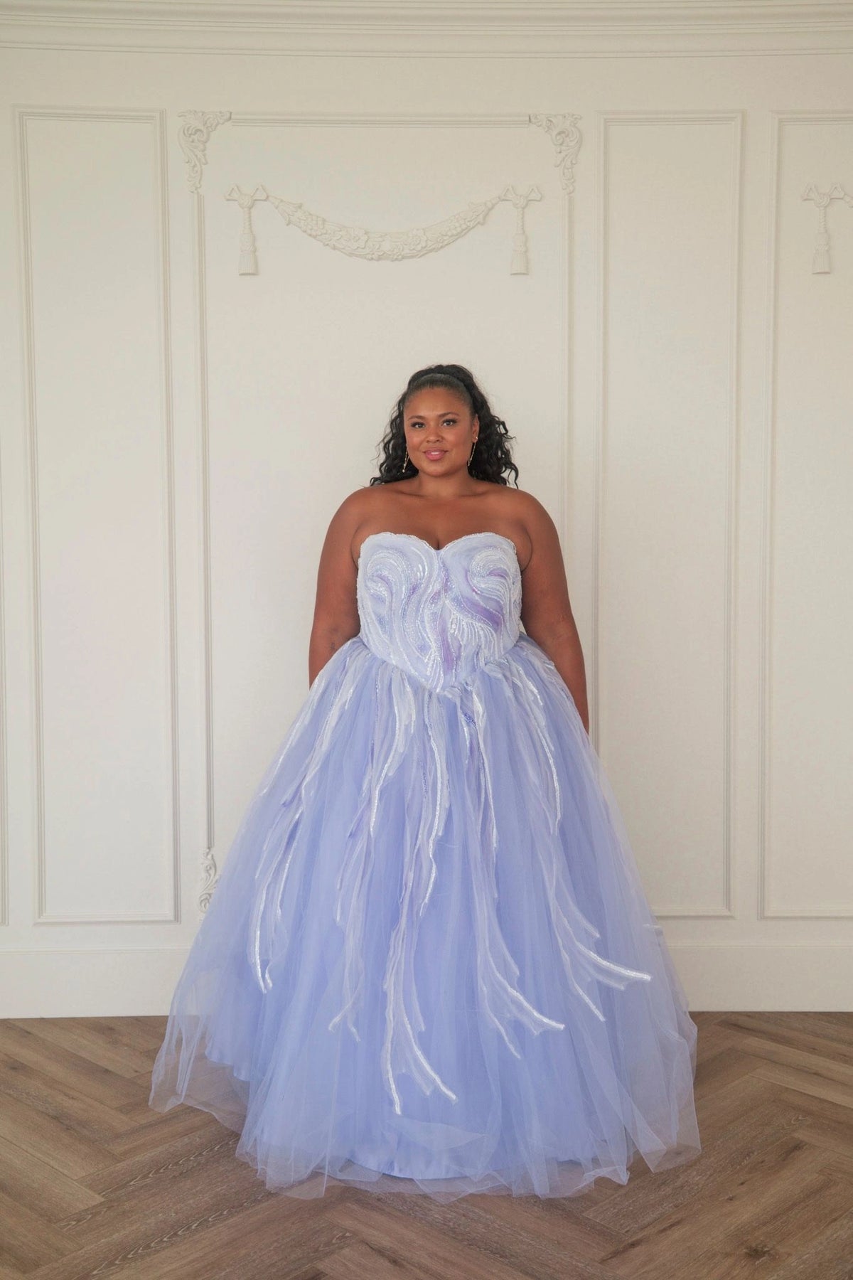 The image shows a woman in a beautiful blue wedding dress standing in front of a white wall, with a watermark in the bottom right corner.